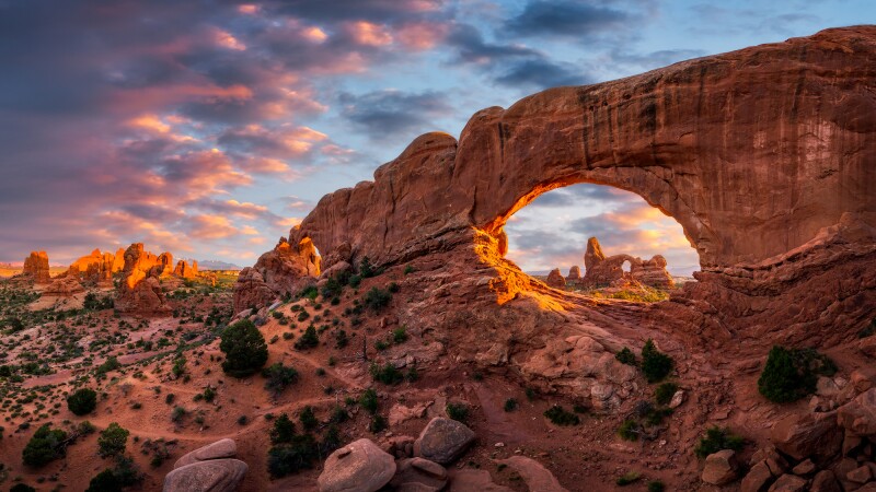 Red rock formations in Utah's Arches National Park at sunset, with one large arch framing another in distance