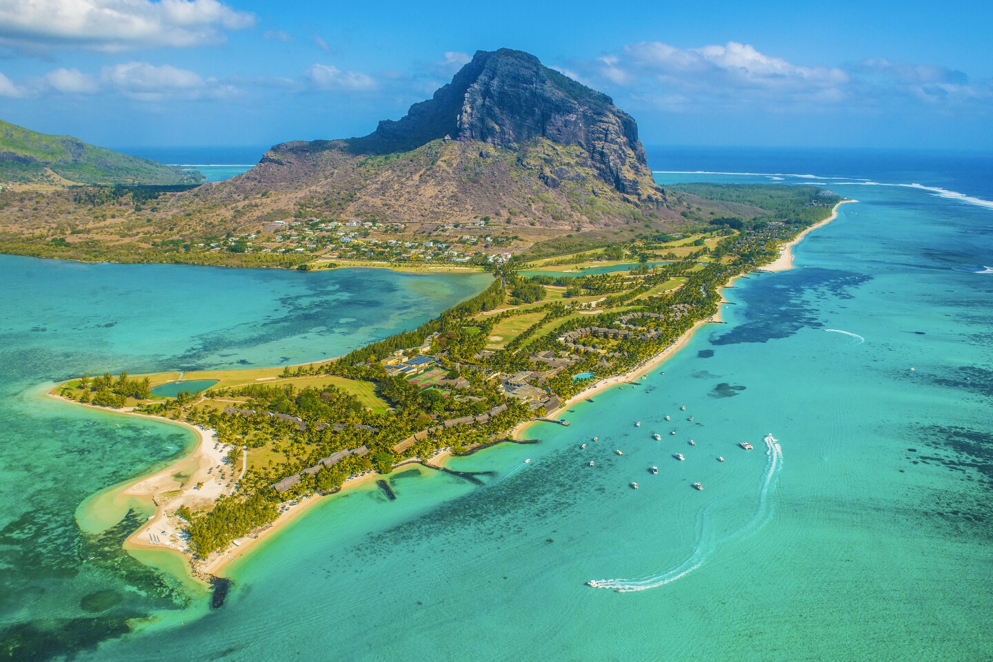Aerial view of green peninsula surrounded by ocean water, with mountain in background