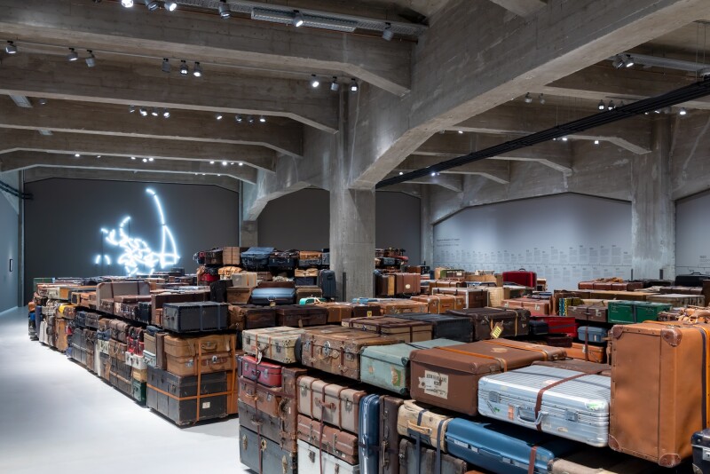A museum gallery filled with piles of suitcases set up in a labyrinth-like pattern