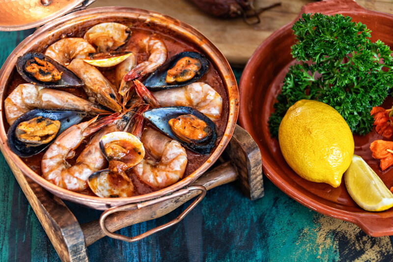 Un cuenco de cobre con gambas enteras, con unos mejillones, junto a un cuenco de perejil y limón.