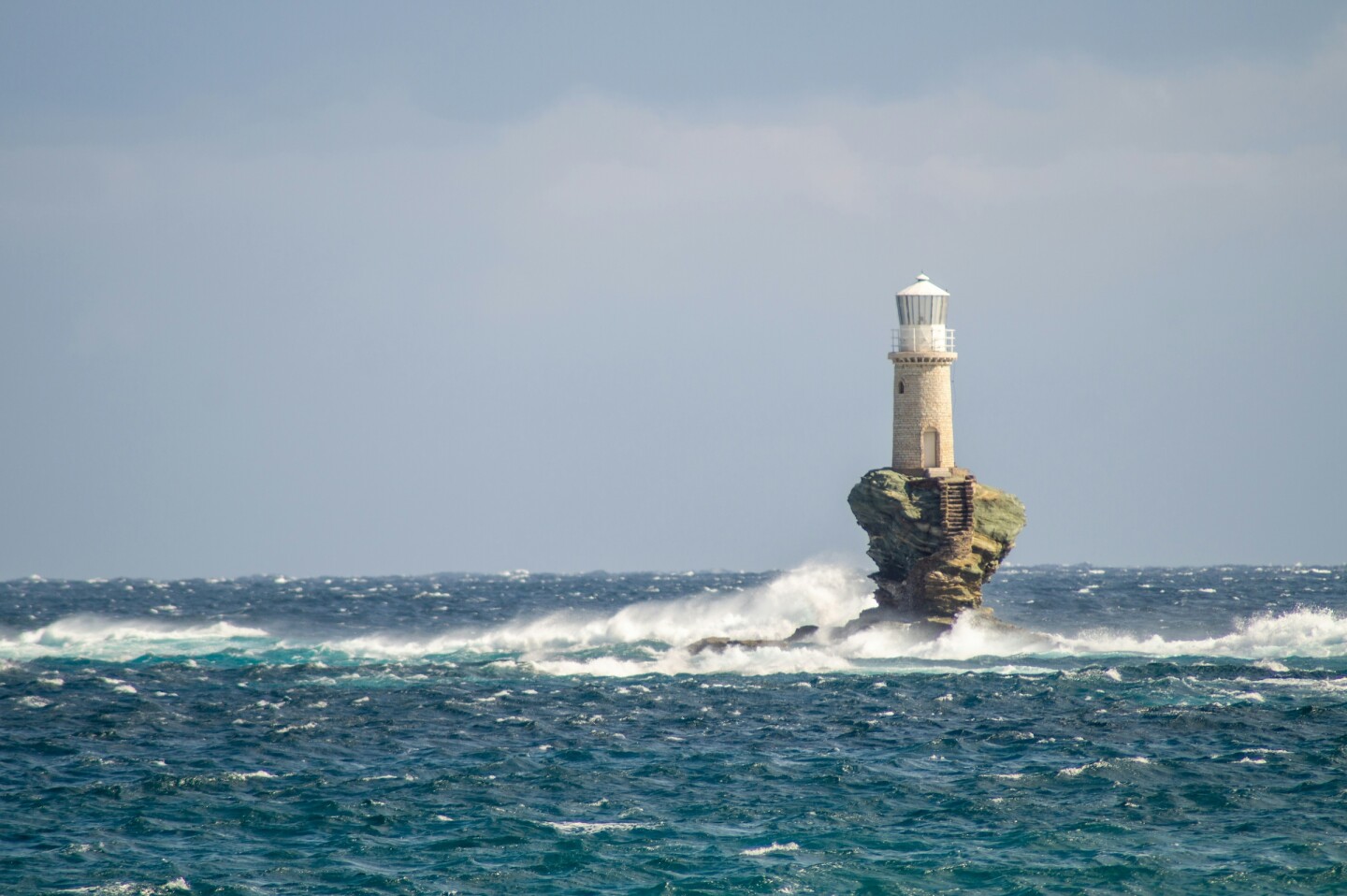 A small lighthouse on a tiny island surrounded by waves