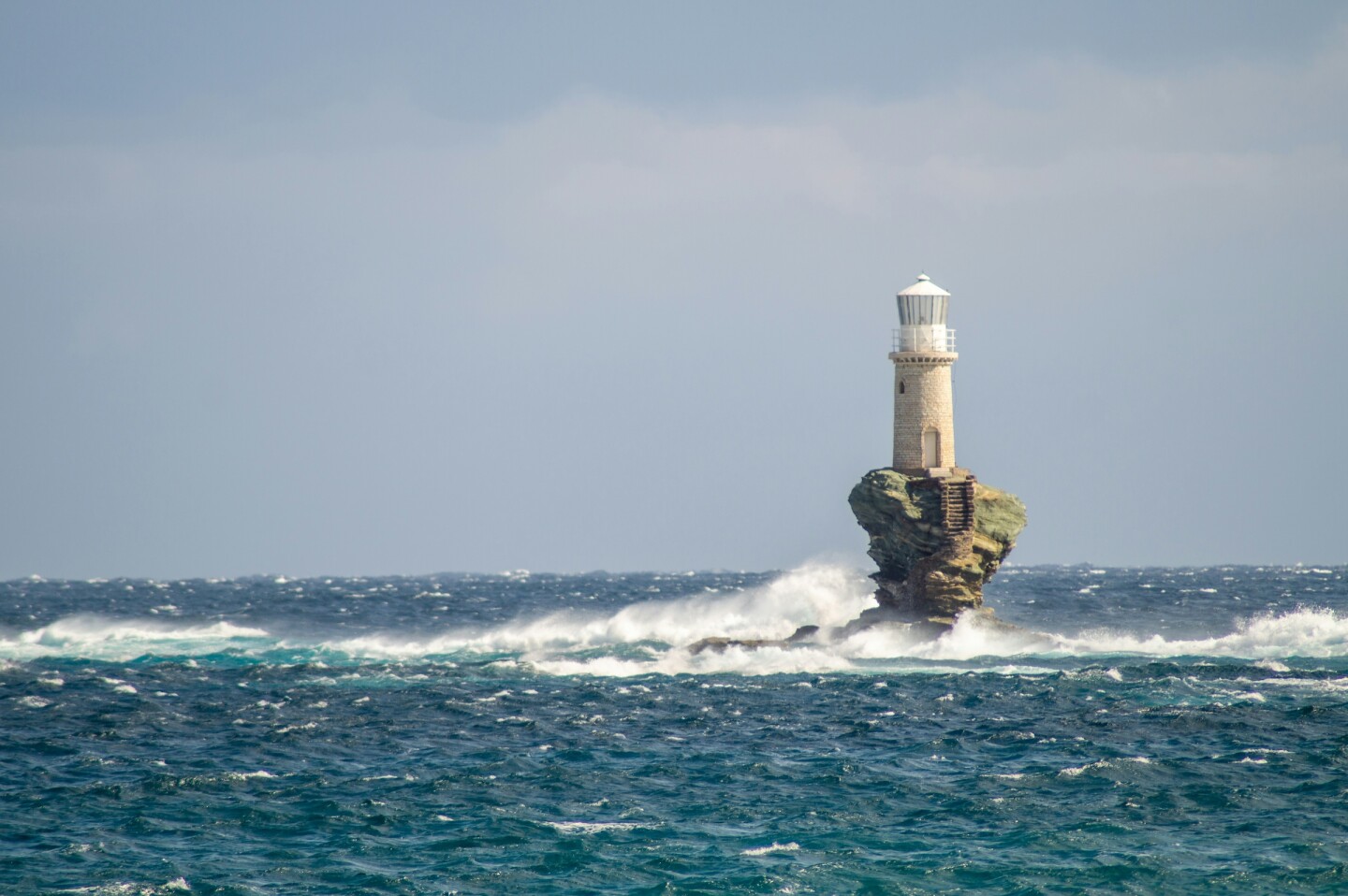 A small lighthouse on a tiny island surrounded by waves 