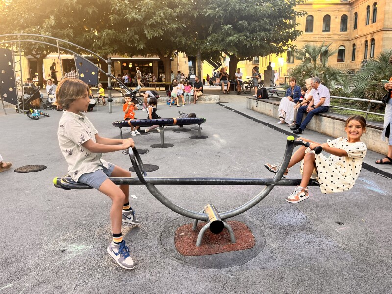 Two kids on a see-saw in a playground full of children in San Sebastián, Spain