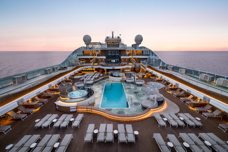A sunset overhead view of outdoor pool deck, with rectangular pool flanked by two hot tubs and numerous empty lounge chairs