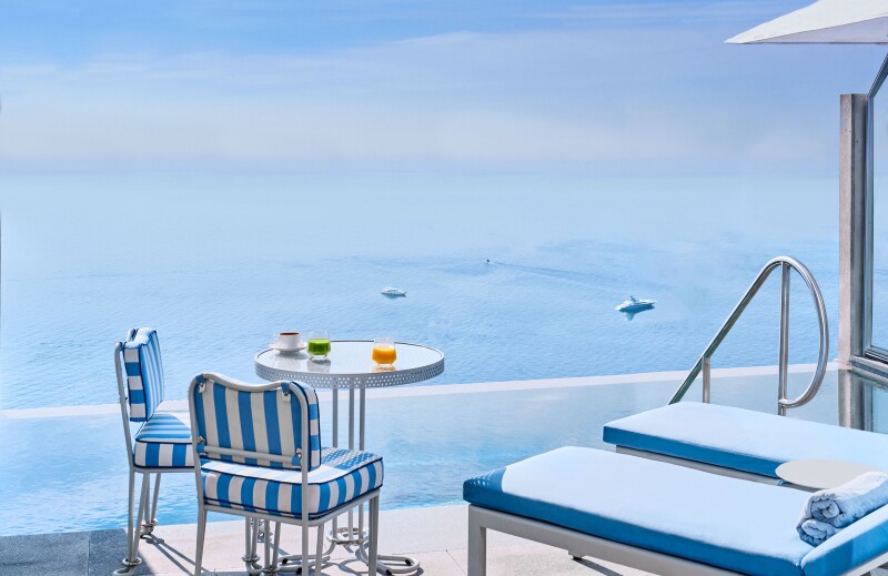 View of Mediterranean from deck of duplex pool suite at the Maybourne Riviera; deck has two blue- and-white striped chairs at small round table, plus two blue lounge chairs