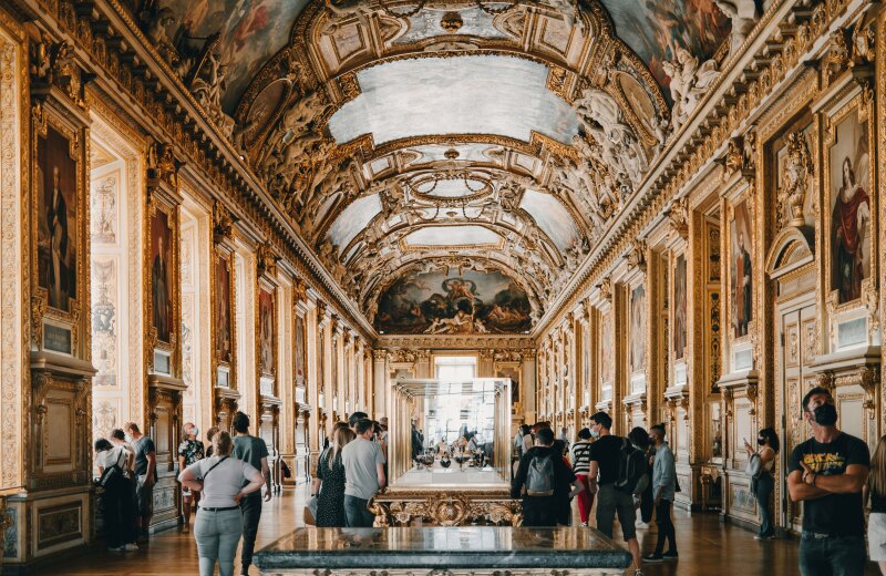 People roaming wide baroque hall in Louvre Museum, with arched ceiling