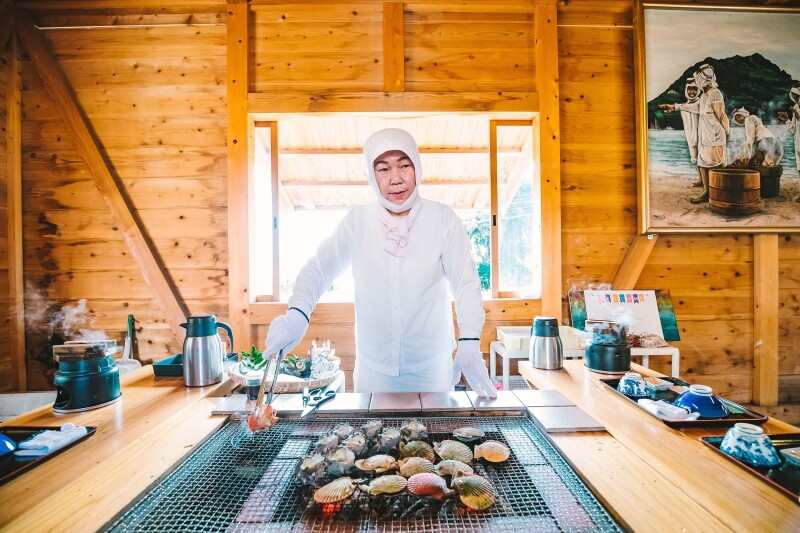 A woman grilling seafood at Ama Hut Satomian