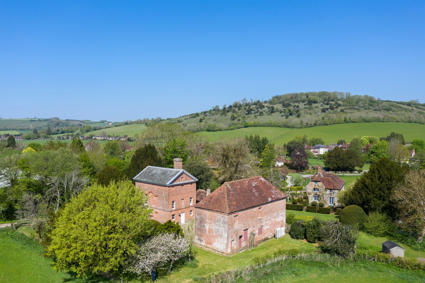 ساختمان های آجری قرمز احاطه شده توسط درختان با تپه های غلتشی در پس زمینه