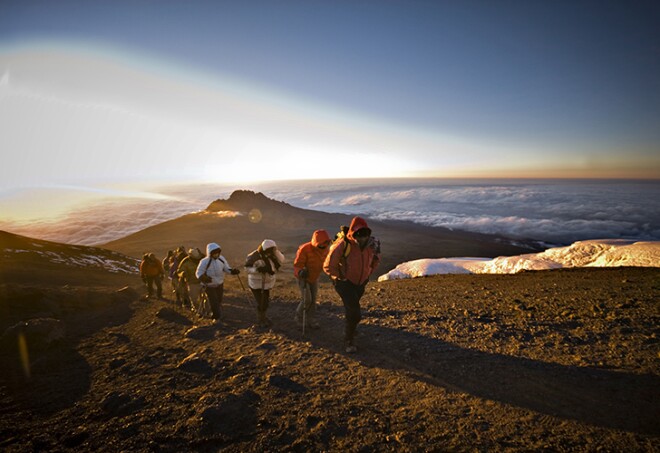 A team of hikers approach the summit of Mt. Kilimanjaro at sunrise after trekking six hours through the night.