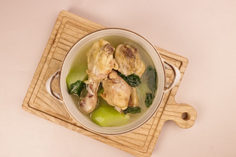 Overhead view of pot of soup with chicken legs and green squash on a wooden cutting board