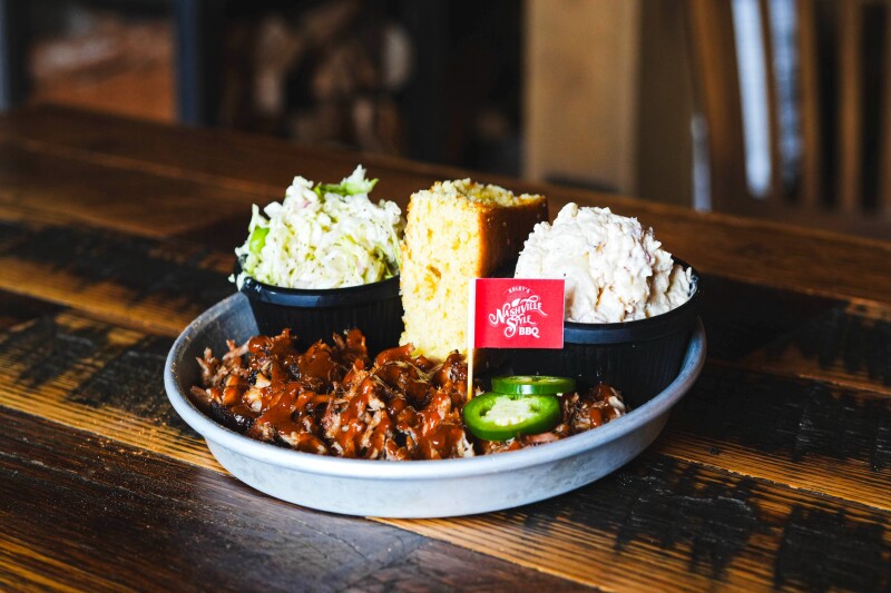 A plate of barbecue, with cornbread, rice, and coleslaw, on a wooden table
