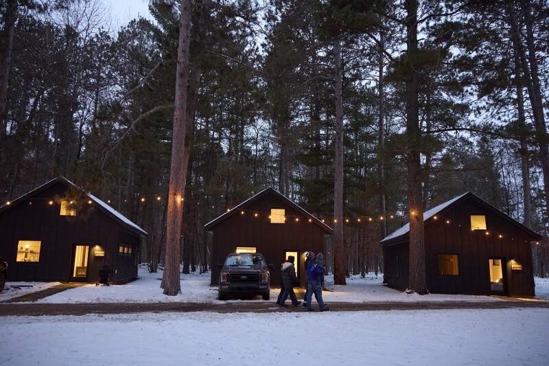A row of cabins in on snow-covered, tree-filled grounds at Nature Link in Nisswa, Minnesota.