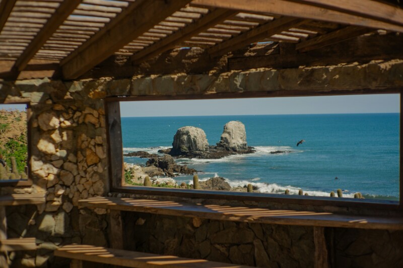 A view of the ocean at Punta de Lobos, Pichilemu, Chile through an outdoor shade structure made of wood and stone.