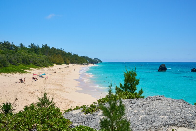 A long stretch of beach edged by greenery and the bright blue water of Warwick Long Bay