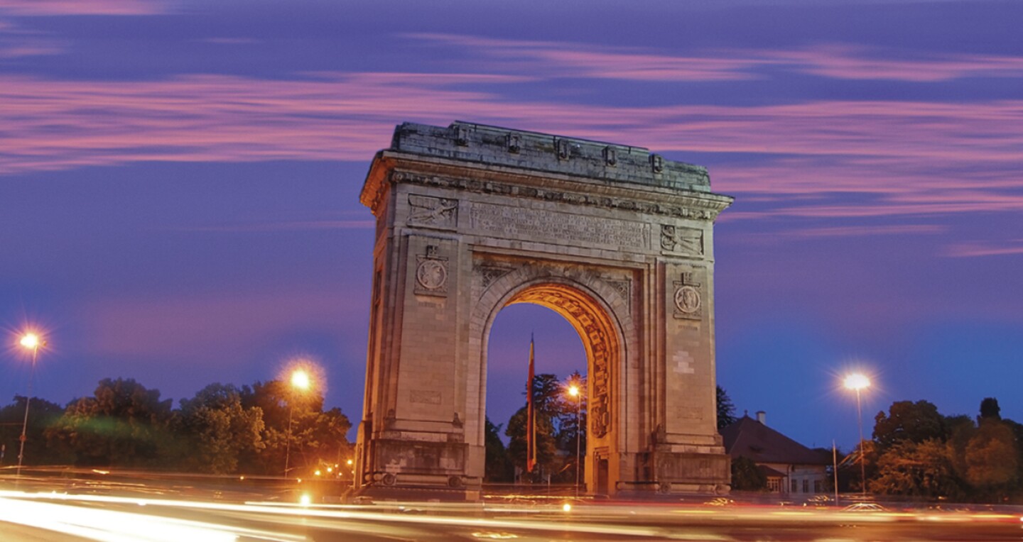 A stone arch on the other side of a street at night.