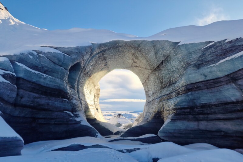 A natural tunnel through an ice cave atop Katla Volcano, with snow and ice in foreground and background