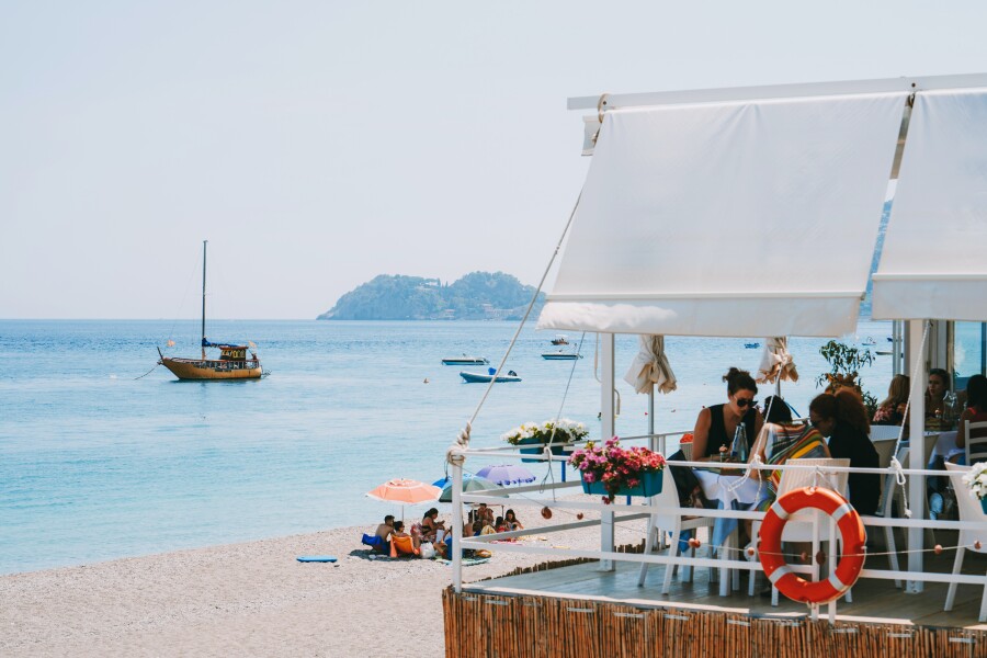 People sit on a covered outdoor patio overlooking the beach and blue ocean water