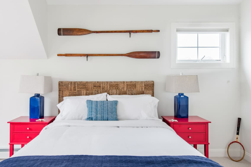 White bedroom with red and blue accents and two oars on wall behind bed