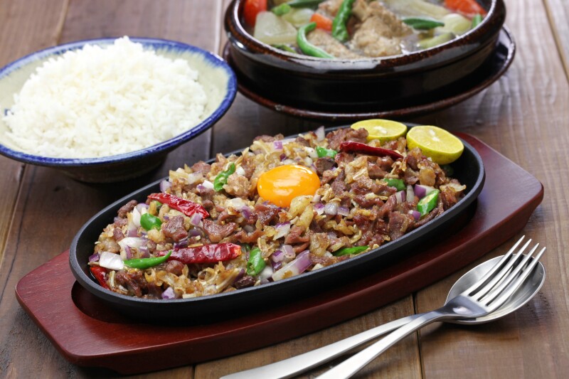 Plate of brown meat with a raw egg yolk on top, beside a bowl of rice