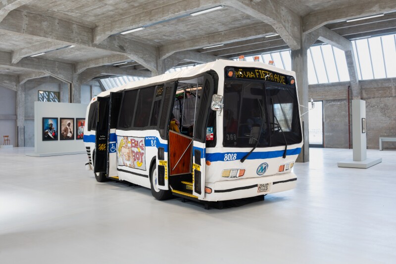 An oversized interactive sculpture that looks like a city bus in a concrete art gallery
