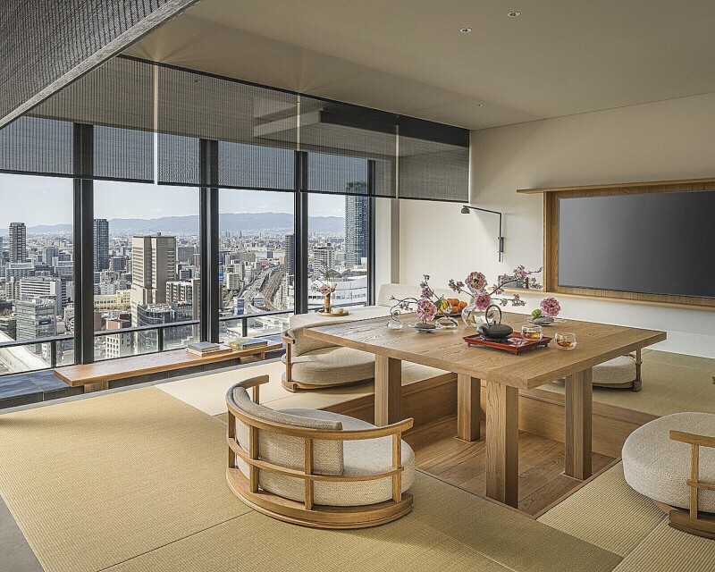 A blonde wood table surrounded by four chairs in the center of a guest room at the Four Seasons Hotel Osaka, with blond wood interiors and views of the city