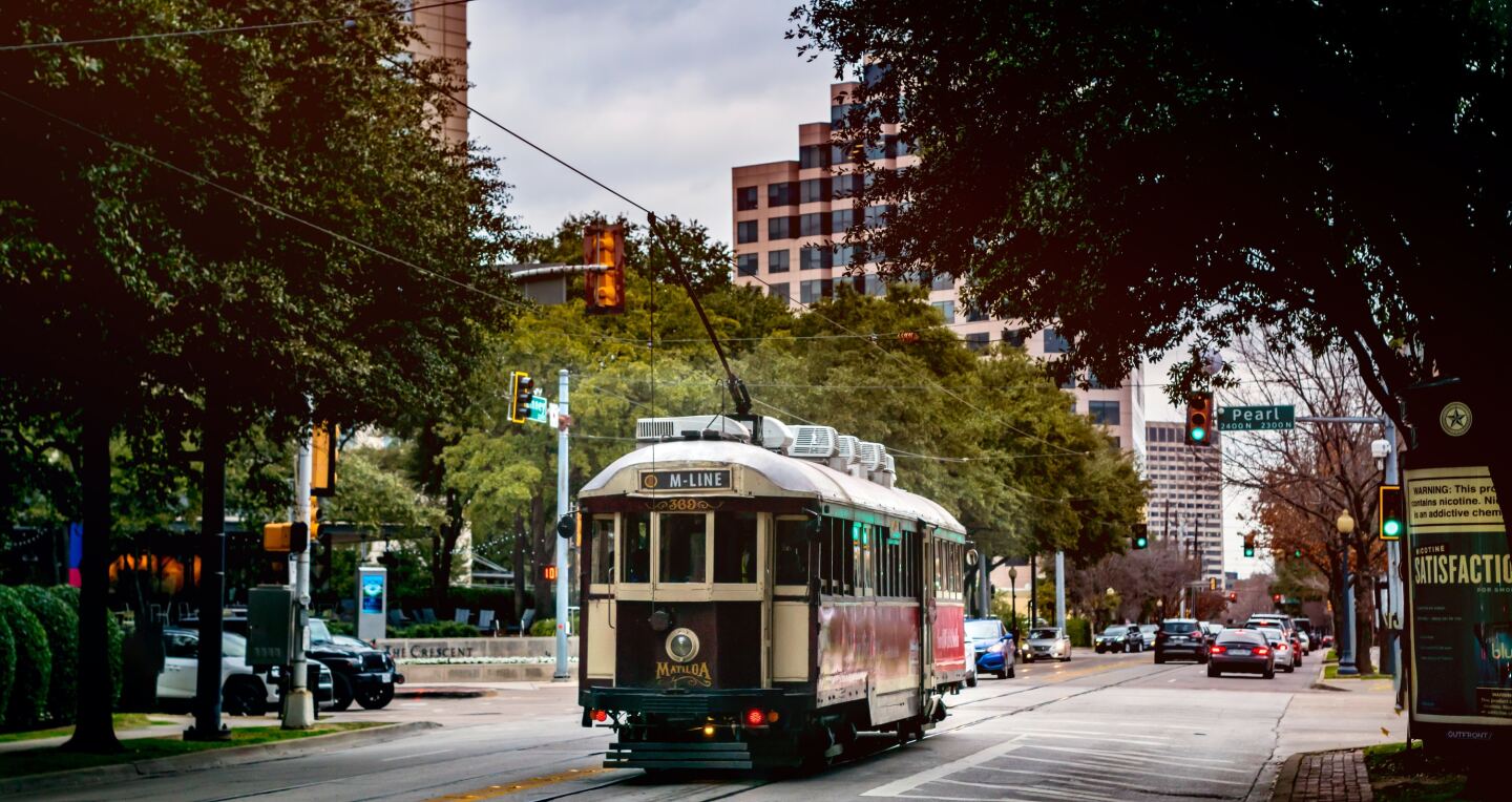 An M-Line trolly moving down the middle of a tree-lined road in Dallas, Texas