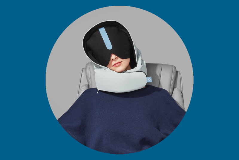 Woman wearing a gray Pluto Pod travel pillow with large, dark eye mask