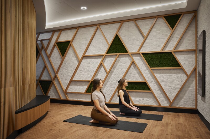 Two people kneeling on dark mats inside yoga room at the Club at SFO, with geometric designs on wall