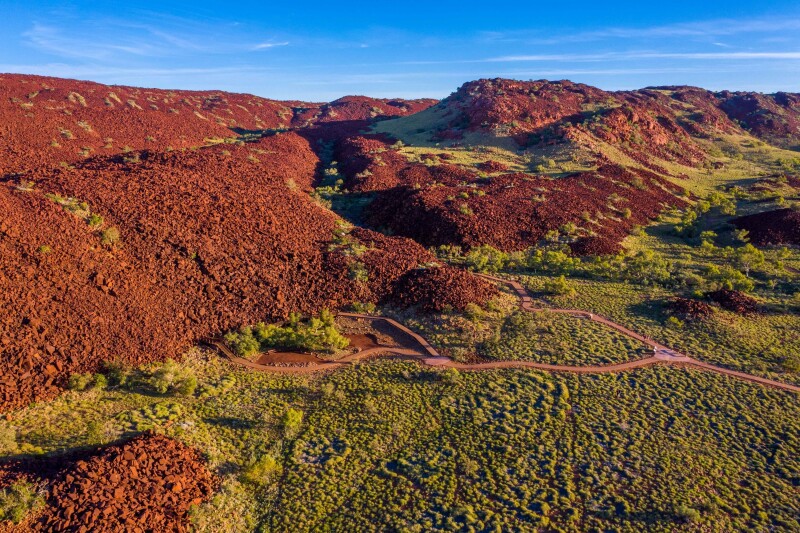 Aerial view of Western Australia's Murujuga National Park, featuring deep red-brown rocky mountains and lime-green flora with several trails snaking through the landscape