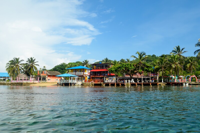 Distant view of houses lining waterfront on Isla Colon, backed by palm trees
