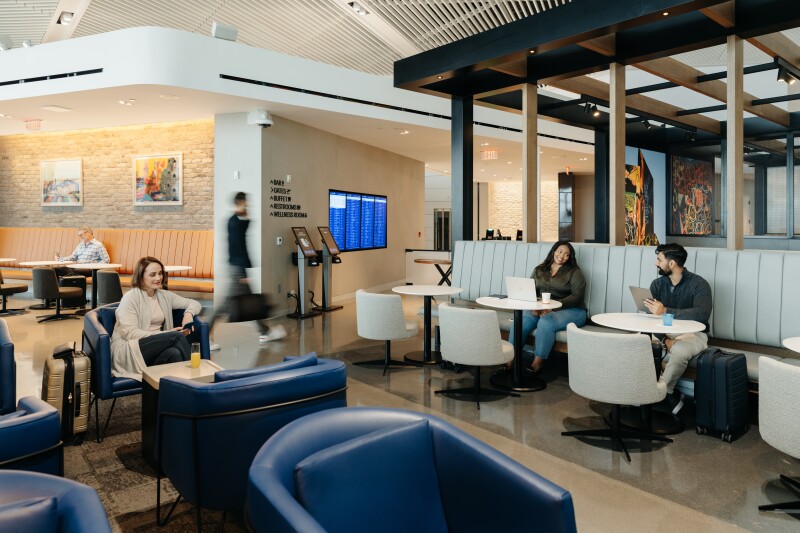 Passengers sitting on blue arm chairs and white banquettes at the United lounge at Newark airport