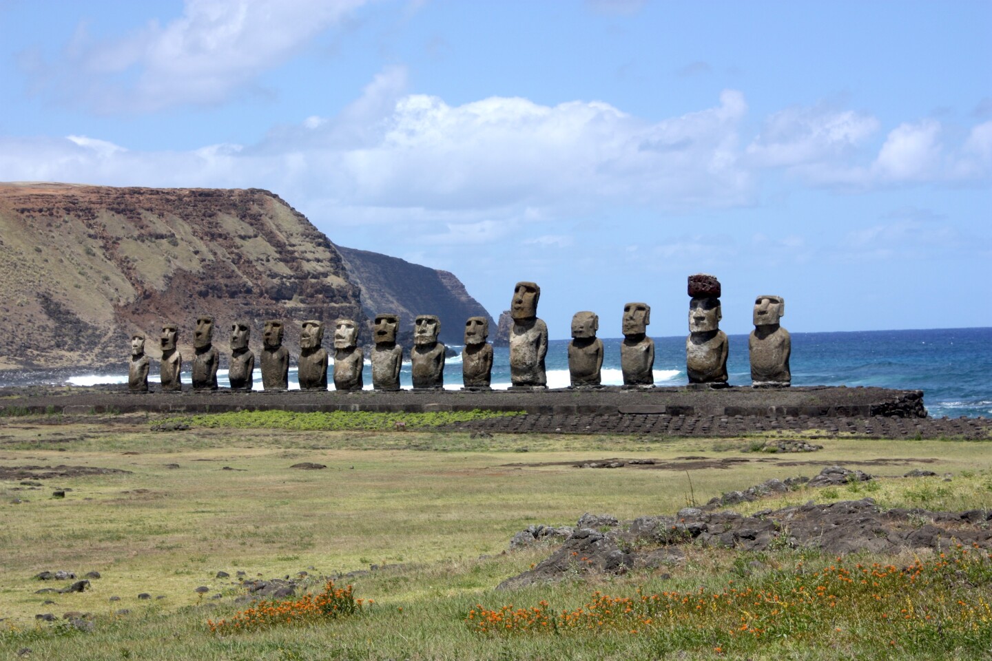 Row of more than a dozen enormous stone head sculptures on stone platform backed by Pacific Ocean, with faces turned inland