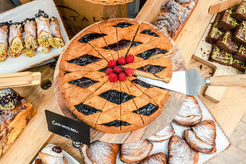 Round crostata sliced into wedges on display table, with assortment of smaller pastries below