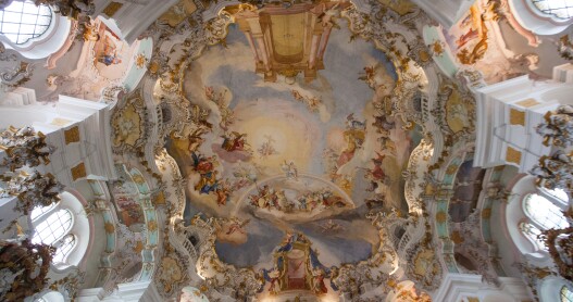 The  painted, gilded, curved ceiling, of the Wieskirche in Germany, flanked by ornate columns and sculptures.