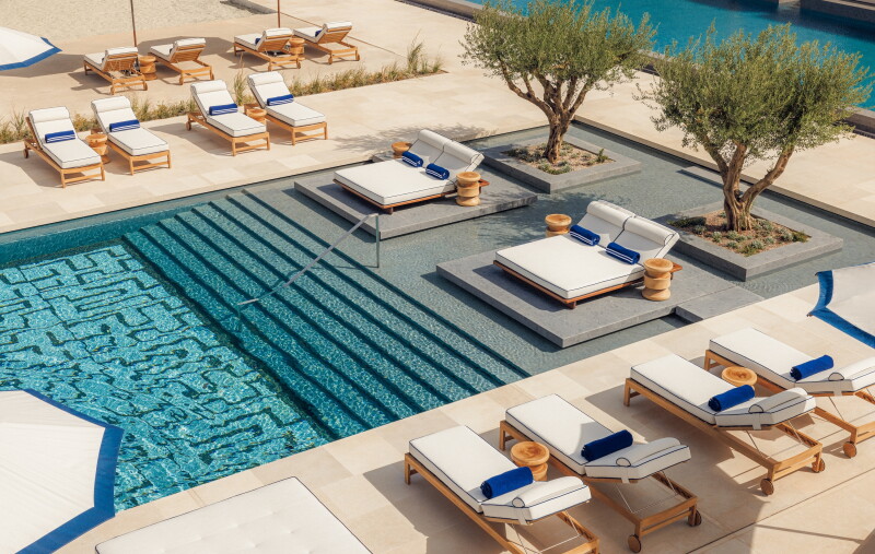 Overhead shot of tiled pool with steps and lined with white-cushioned wooden lounge chairs, plus two olive trees