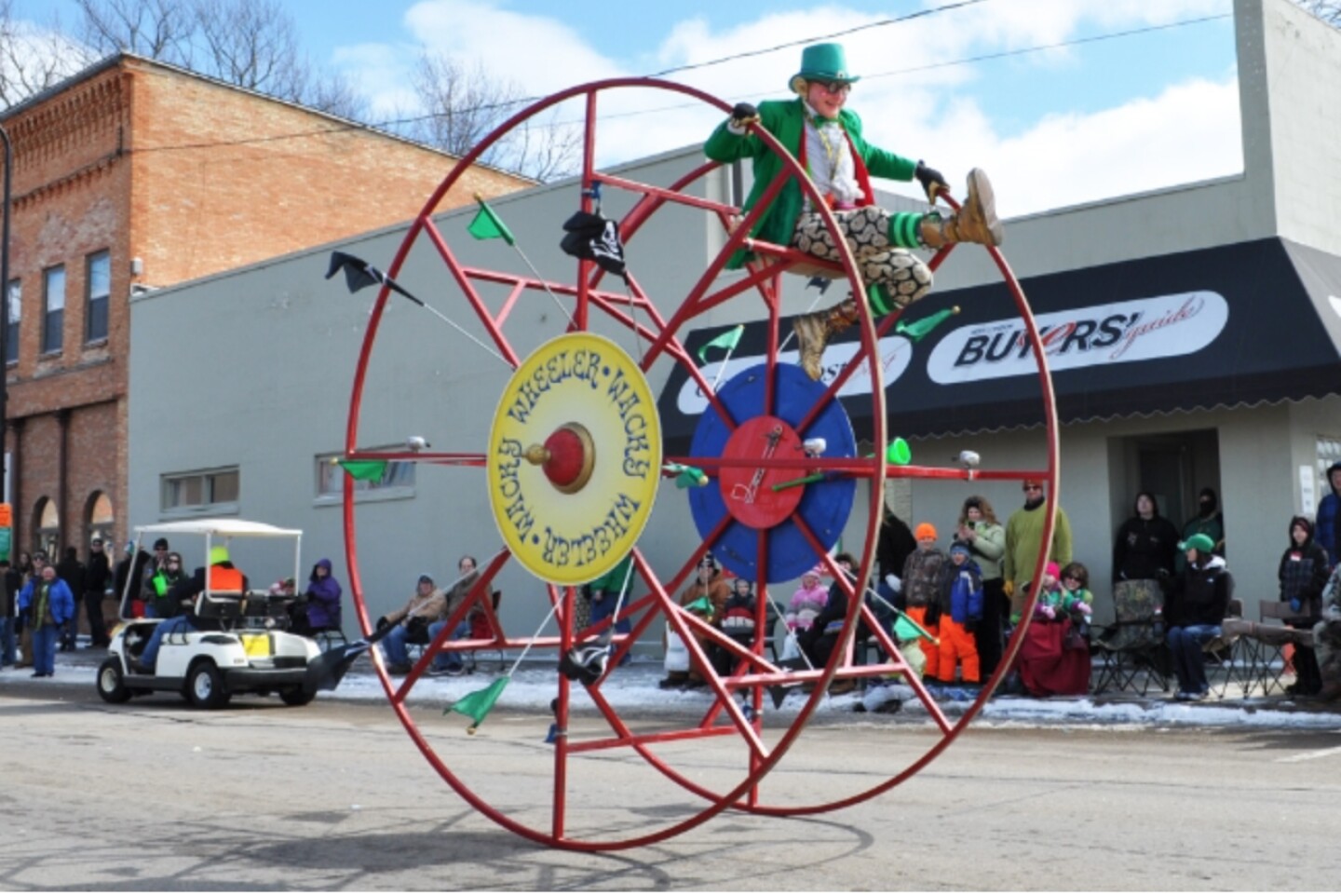 A local “leprechaun” riding between two large red wheels on street in New London