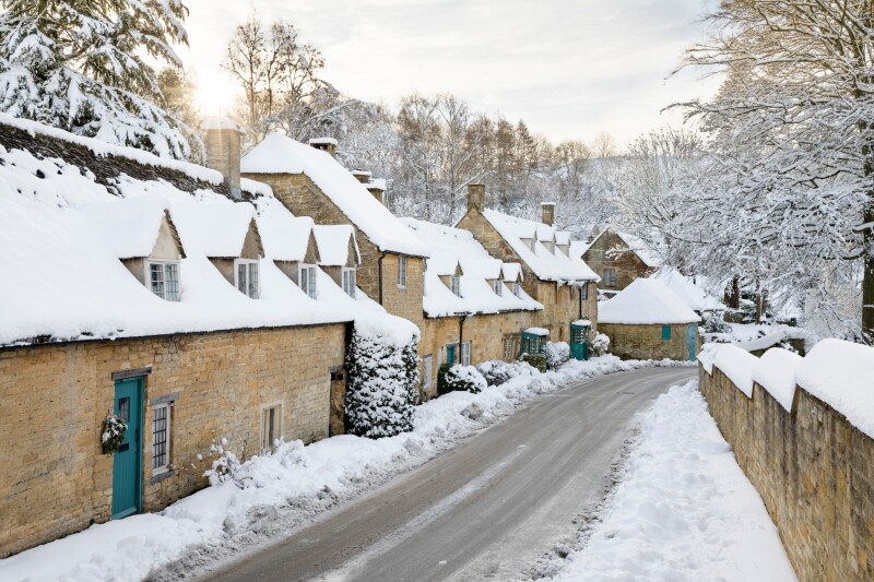 Line of stone cottages covered in winter snow alongside narrow road