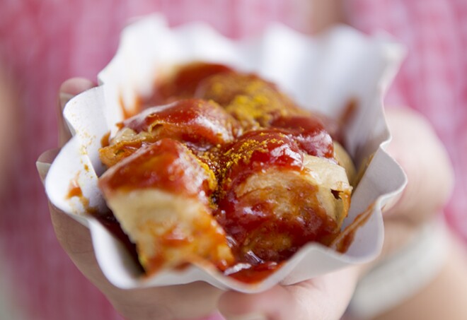 Frau vor Konnopke's Imbiss mit Currywurst in der Hand