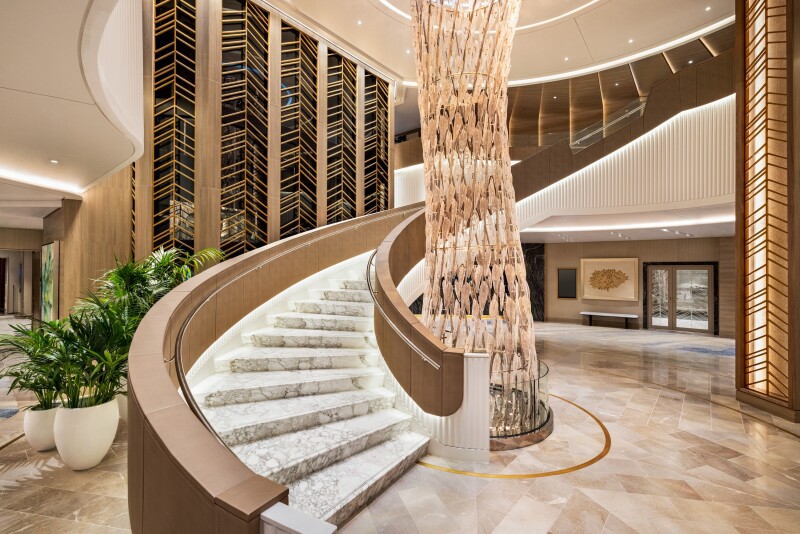 A twisting floor-to-ceiling chandelier next to curving staircase and central atrium area