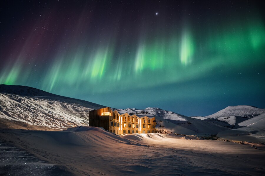 Three-story hotel building in the middle of a snowy landscape with the northern lights overhead