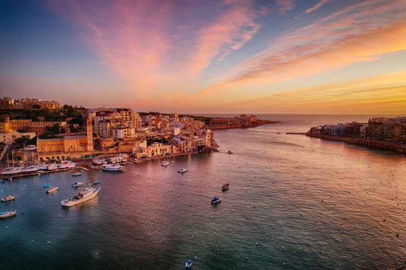 Sunset over Marsaskala, a seaside town in Malta, with small boats at harbor