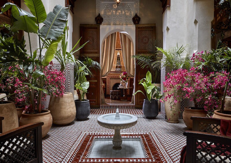 Small interior courtyard with small fountain surrounded by tile floor and green and pink plants in large pots at the Royal Mansour in Marrakech