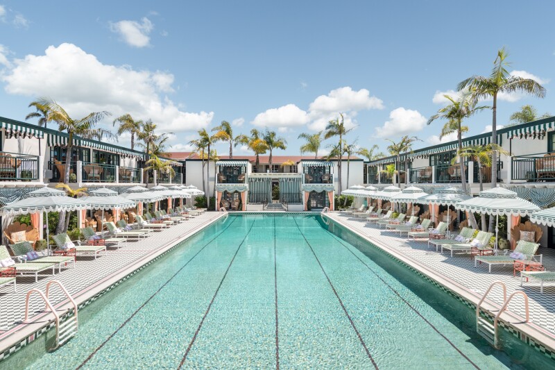 A rectangular pool with black-and-white tiles and pink ladders, lined with lounge chairs under palm trees and fringed umbrellas