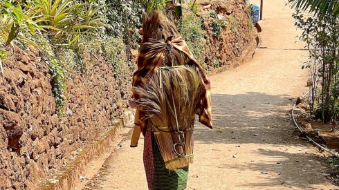 A woman walks through Kongthong Village with brooms on her back