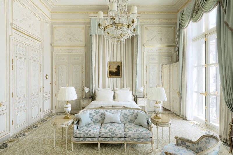 Interior of white Windsor Suite, with sofa at foot of bed, chandelier over it, and large windows