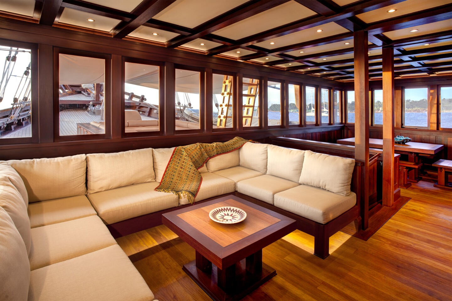 A large, cream-colored sofa in the Dunia Baru lounge, a vessel that sails in Indonesia, with big picture windows all around