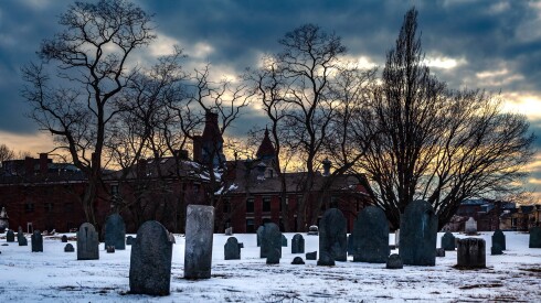 Sunrise over a 17th-century cemetery in Salem, Massachusetts with snow on the ground and bare trees