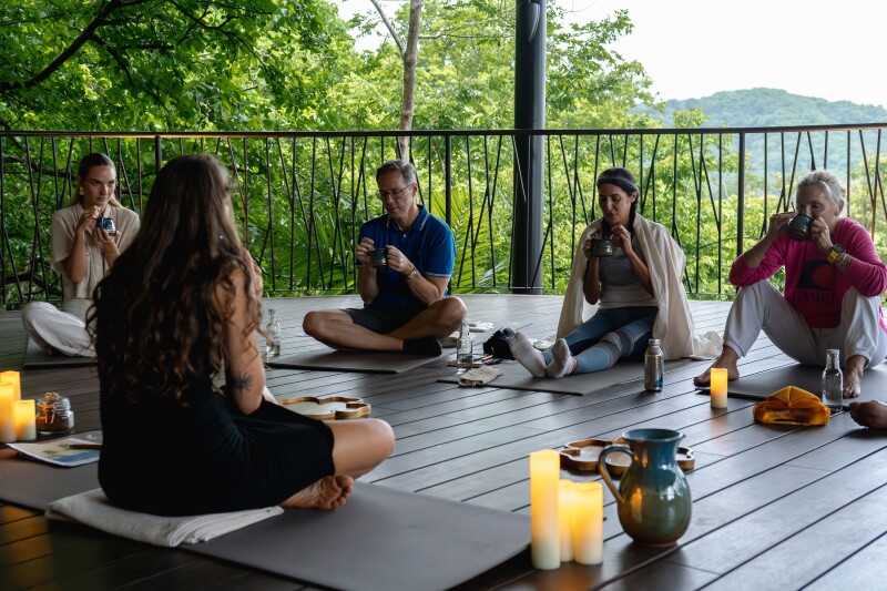 A few students seated on wood floor of open-air pavilion for a cacao ceremony, with several lit candles