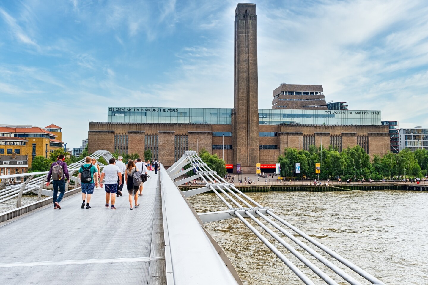 A modern metal pedestrian bridge over River Thames leading to the Tate Modern, an enormous brick building with a tall rectangular tower