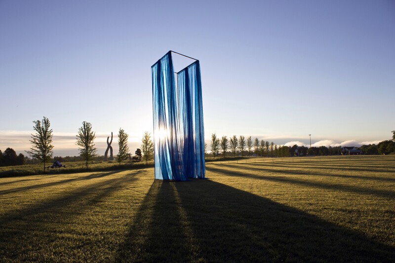 An art installation made from sheets of blue fabric on a grassy patch with the sun shining through from the back
